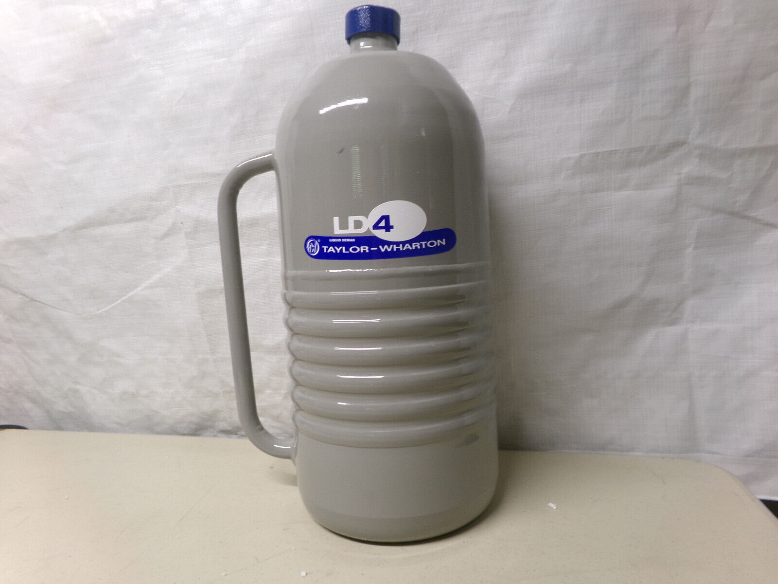 A grey metal canister with a blue cap and handle.